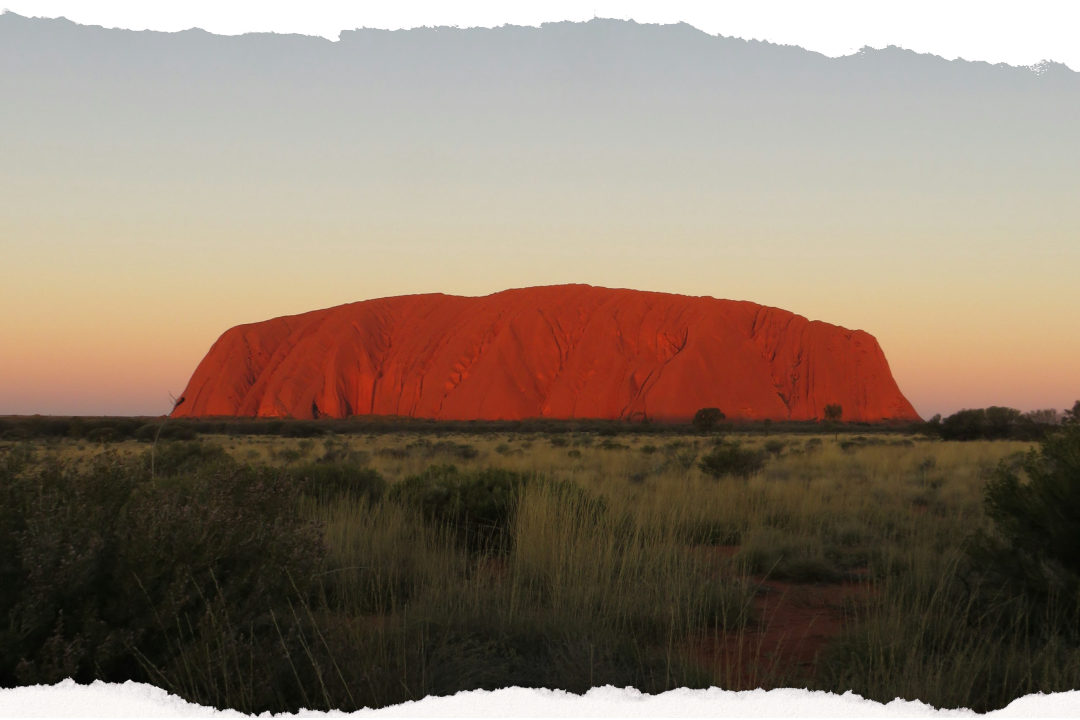 Uluru glowing red at sunset against the desert