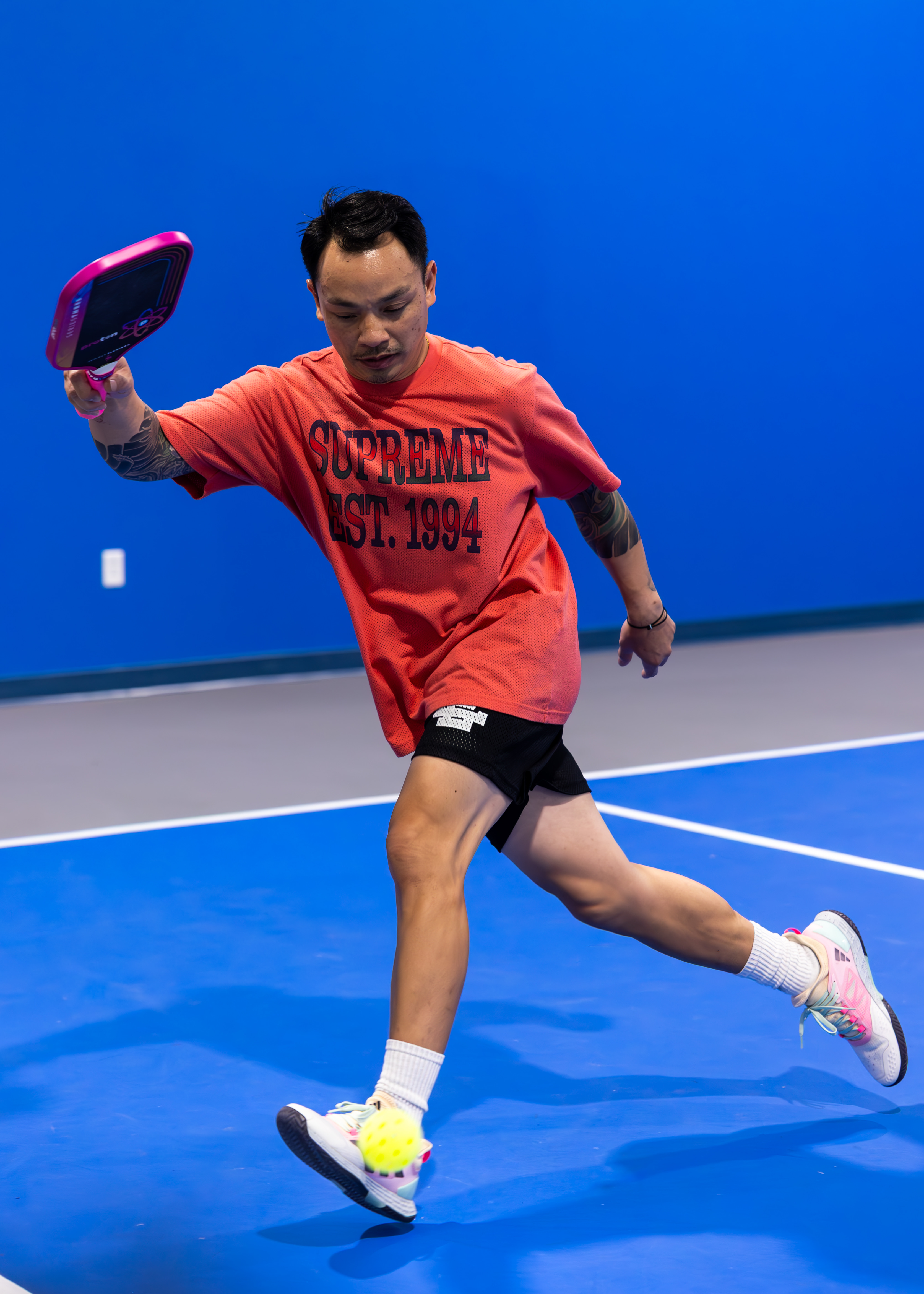 Two people playing pickleball on an indoor court, both focused on the game. The background shows a blue wall and a net. Text in image: Pickleball Kingdom. The mood is energetic and welcoming.