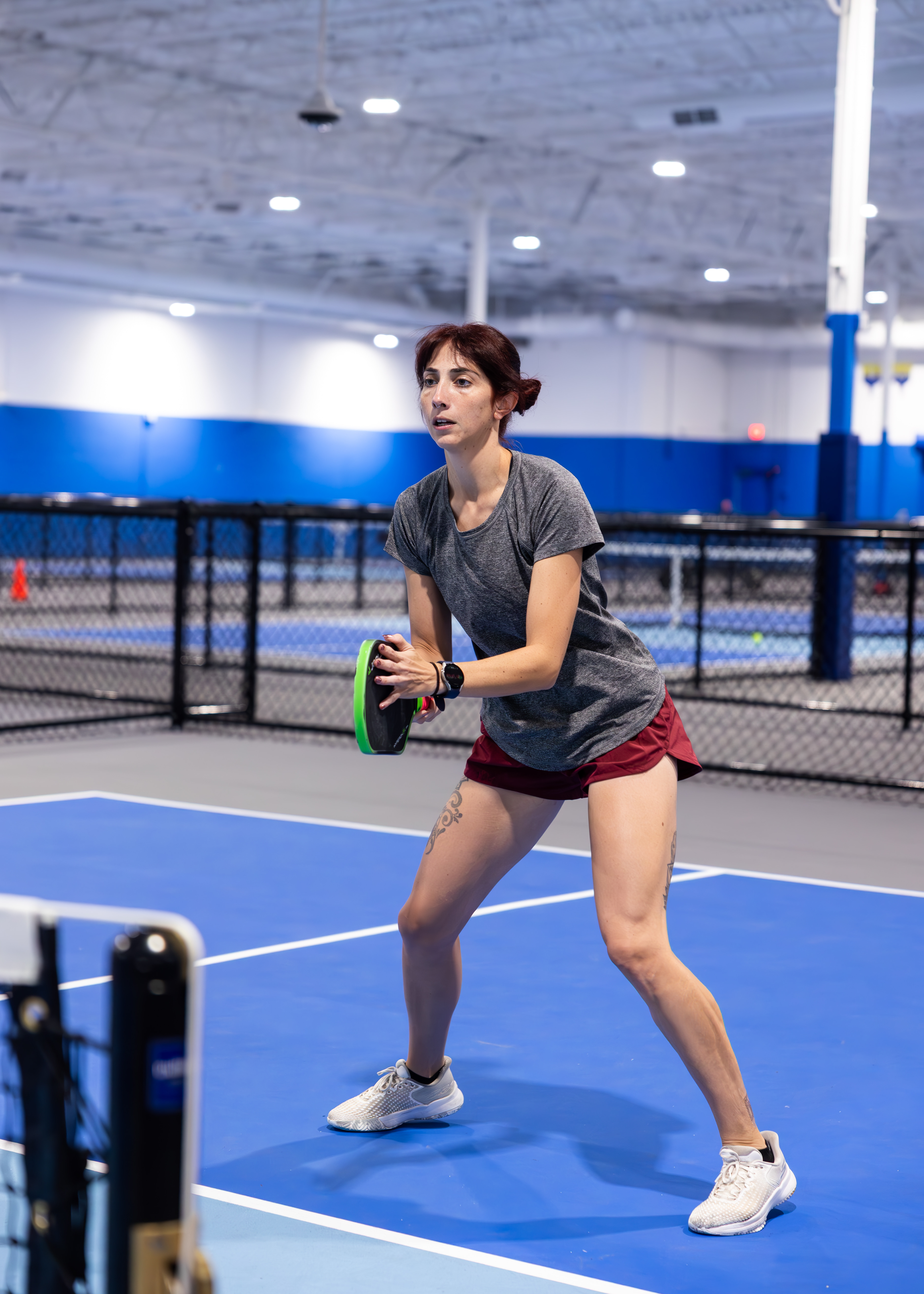 Two people playing pickleball on an indoor court, both focused on the game. The background shows a blue wall and a net. Text in image: Pickleball Kingdom. The mood is energetic and welcoming.