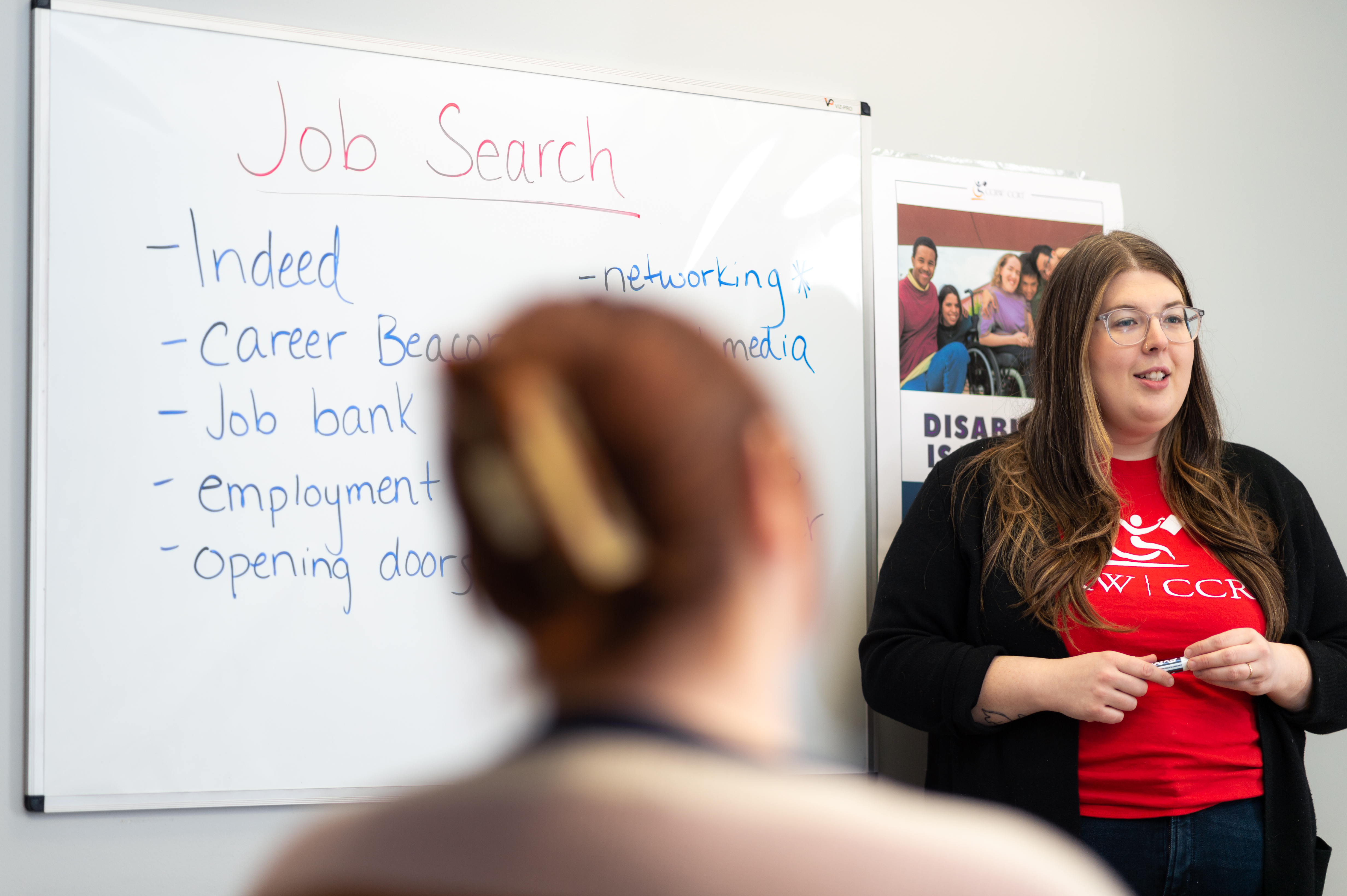 A person in a CCRW t-shirt in front of a white board that says, "Job Search", and lists various job boards.