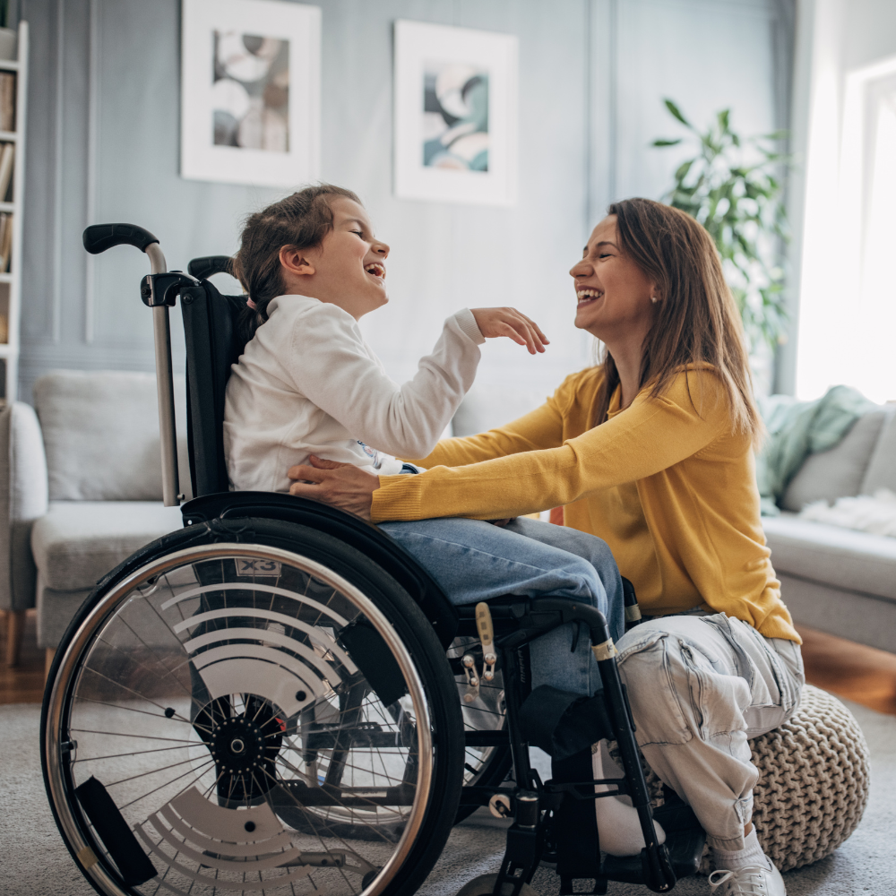 Photo of a mother and young child who is in a wheelchair having fun together in a living room at home.