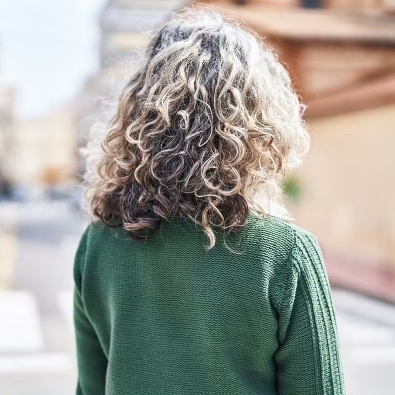 Photo of the back of a woman wearing a green sweater with curly hair