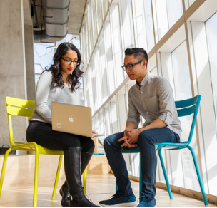 Casual setting, two people seated, looking at one computer
