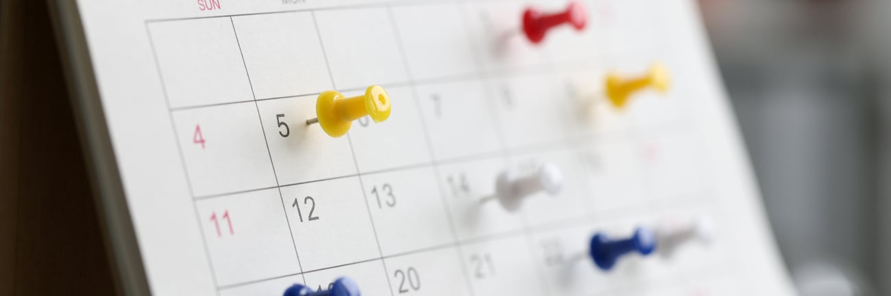 Image of calendar with colourful thumb tacks on different dates on the calendar.