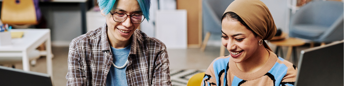 Two people smiling while working on shared computers.