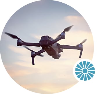 A drone flies in a blue sky scattered with clouds.
