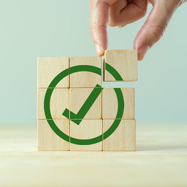 hand moving last of nine wooden block to create image of a large green circle with a check mark inside.