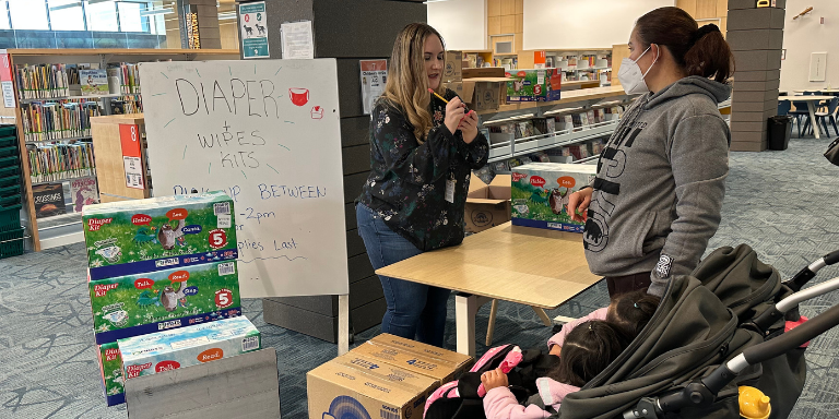 Diaper Kit giveaway at the library. A woman writing on a post-it speaking to a mother of two. Diaper Kit giveaway at the library. A woman
writing on a post-it speaking to a mother of two.