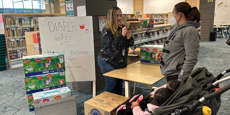 Diaper Kit giveaway at the
library. A woman writing on a post-it speaking to a mother of two.