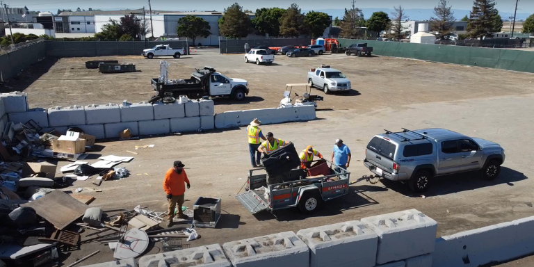 Photo of people unloading a small tow-trailer of junk.