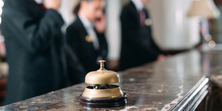 Photo of a bell on a hotel counter with staff on phones in the background.