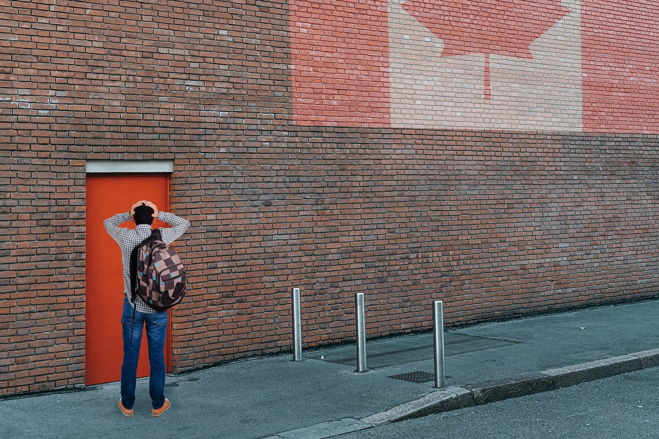 Image of a man standing with his back turned, facing a brick wall. The Canadian flag is being projected on the wall.