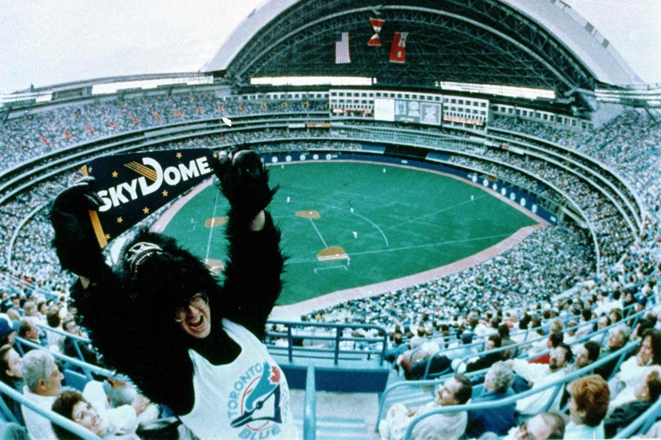 A photo of the first Blue Jays game played at Skydome. In the foreground, a man dressed as a gorilla is holding a sign that reads SkyDome.