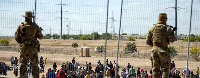 Migrants wait in line adjacent to the border fence under the watch of the Texas National Guard to enter into El Paso, Texas. AP/Andres Leighton, file