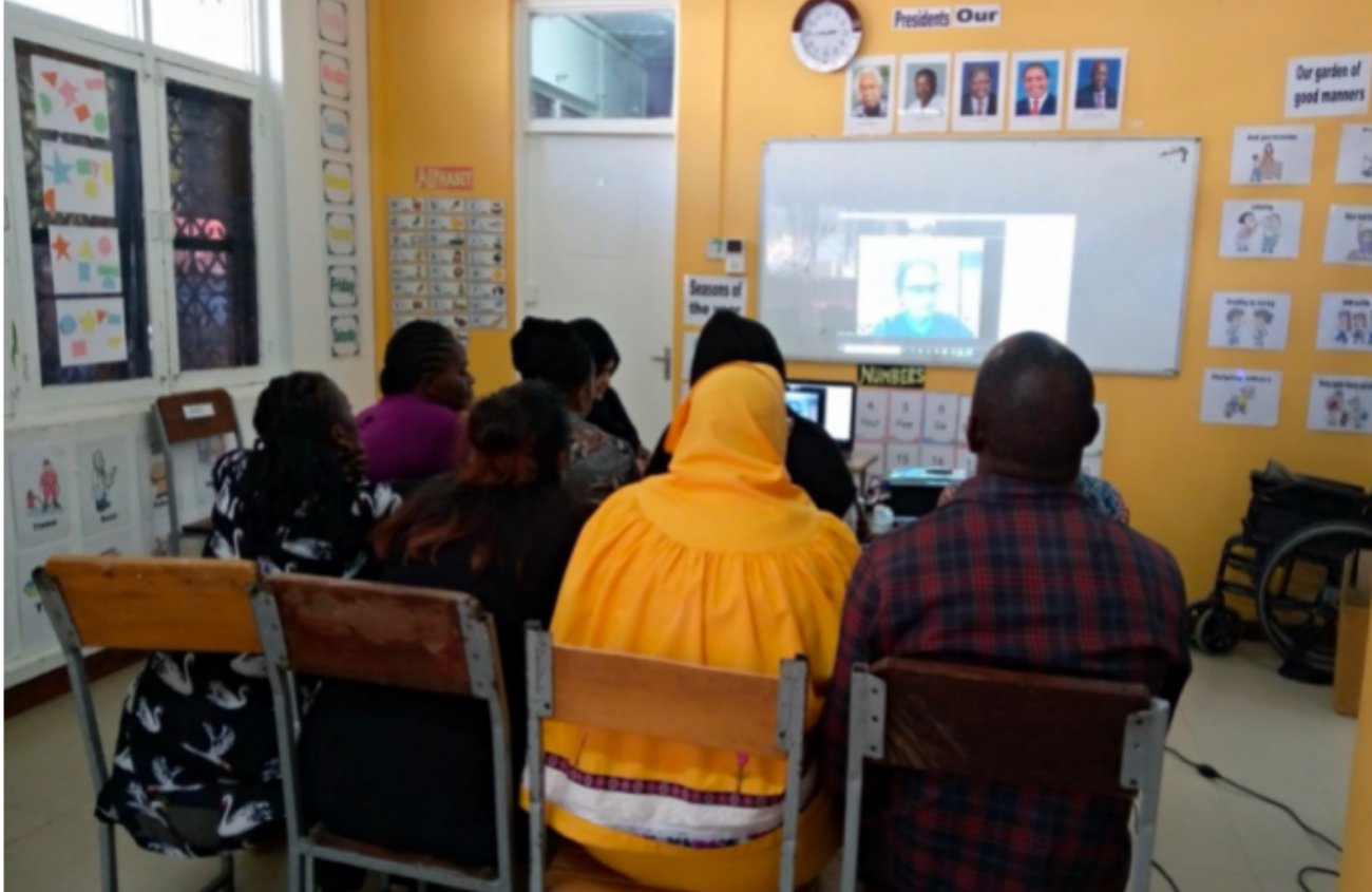 A group of people sitting in chairs in a room watching a webinar projected on a screen.