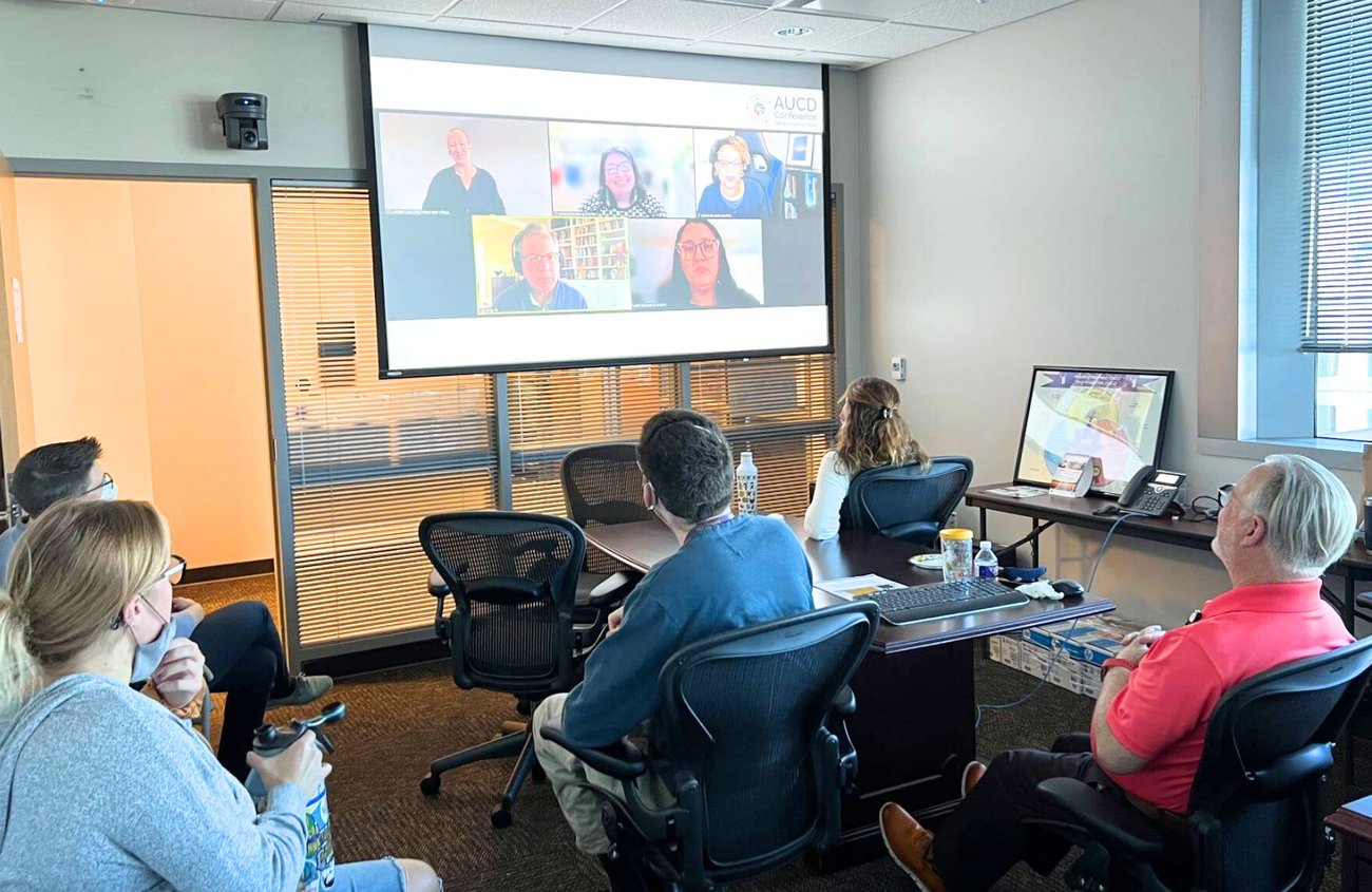 This image shows a computer screen displaying a virtual meeting with five participants in a video call. There is a sign language interpreter in the top right corner, and subtitles at the bottom of the screen read "intellectual and developmental disabilities." The top left corner has a logo with the text "ACHIEVING EQUITY #AUCD2020."