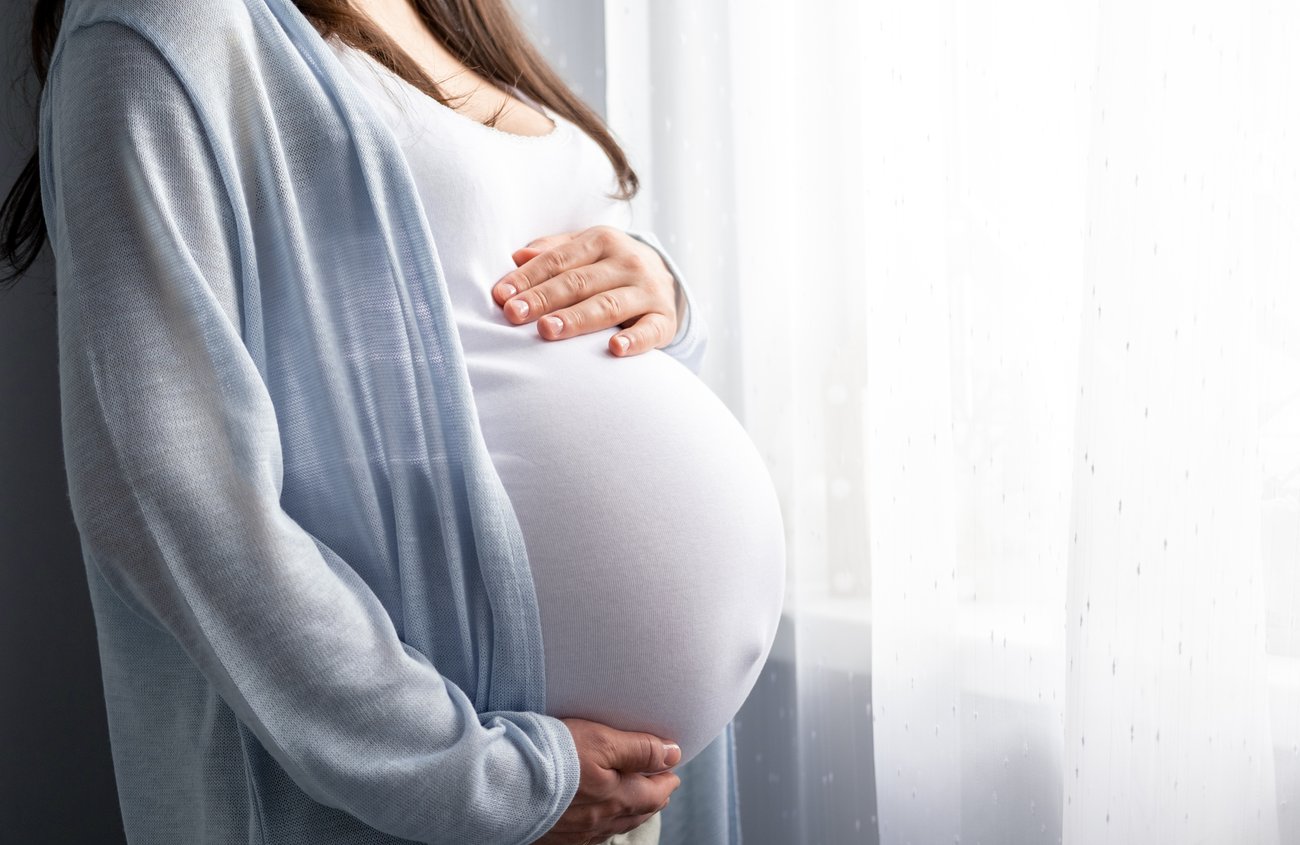 a pregnant woman holds her belly while looking out a window