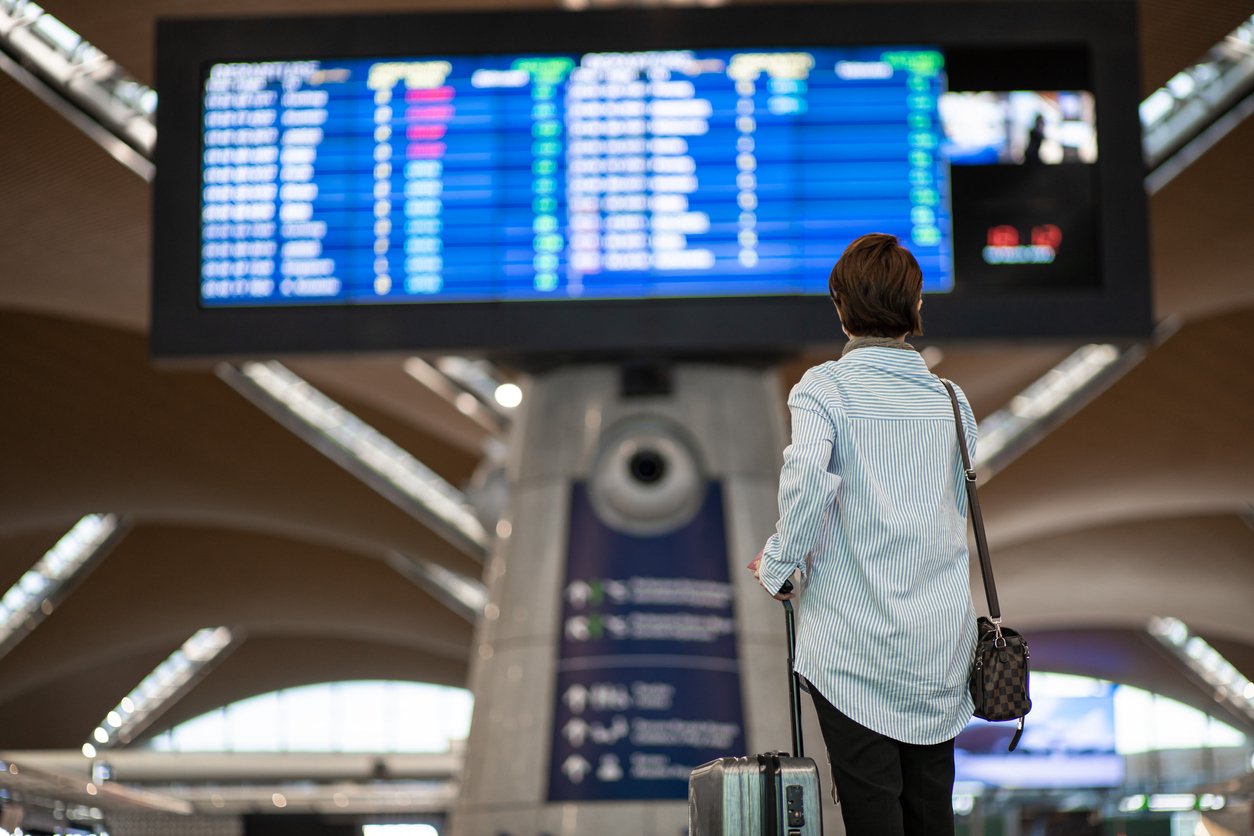 rear view of a female chinese traveler viewing the arrival/departures board at an airport