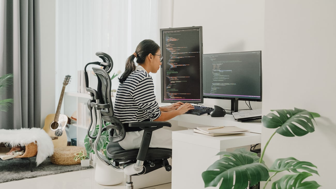 Young Asian woman software developers using computer to write code sitting at desk with multiple screens work remotely at home