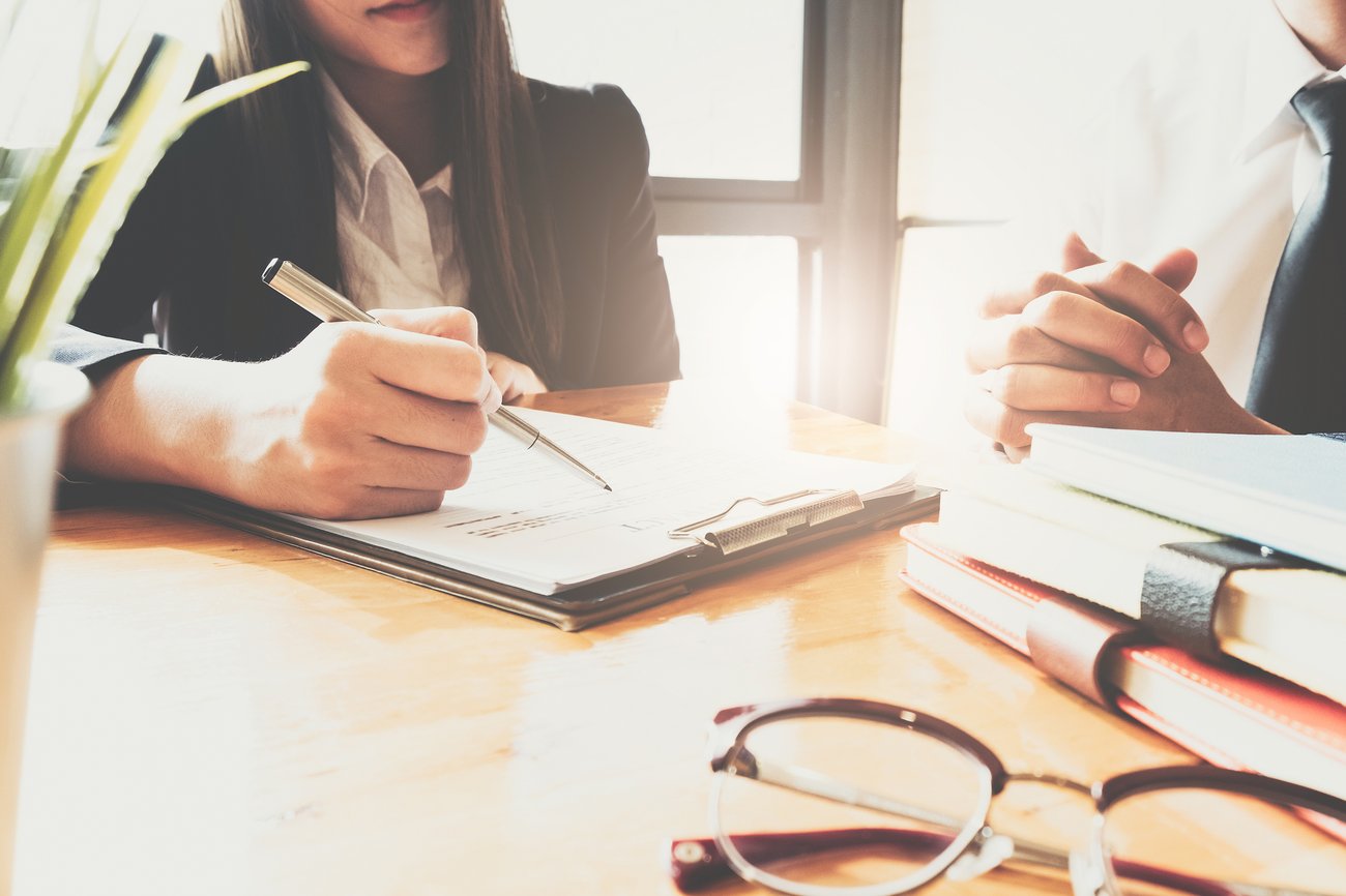 women writing notes onto clipboard, sitting at desk