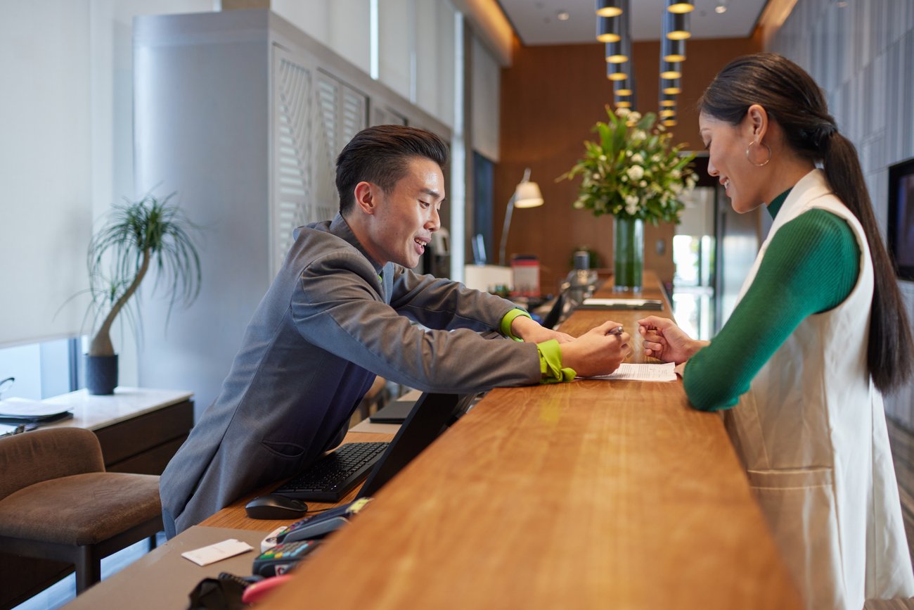 Hotel front desk employee stands from stool to check in guest