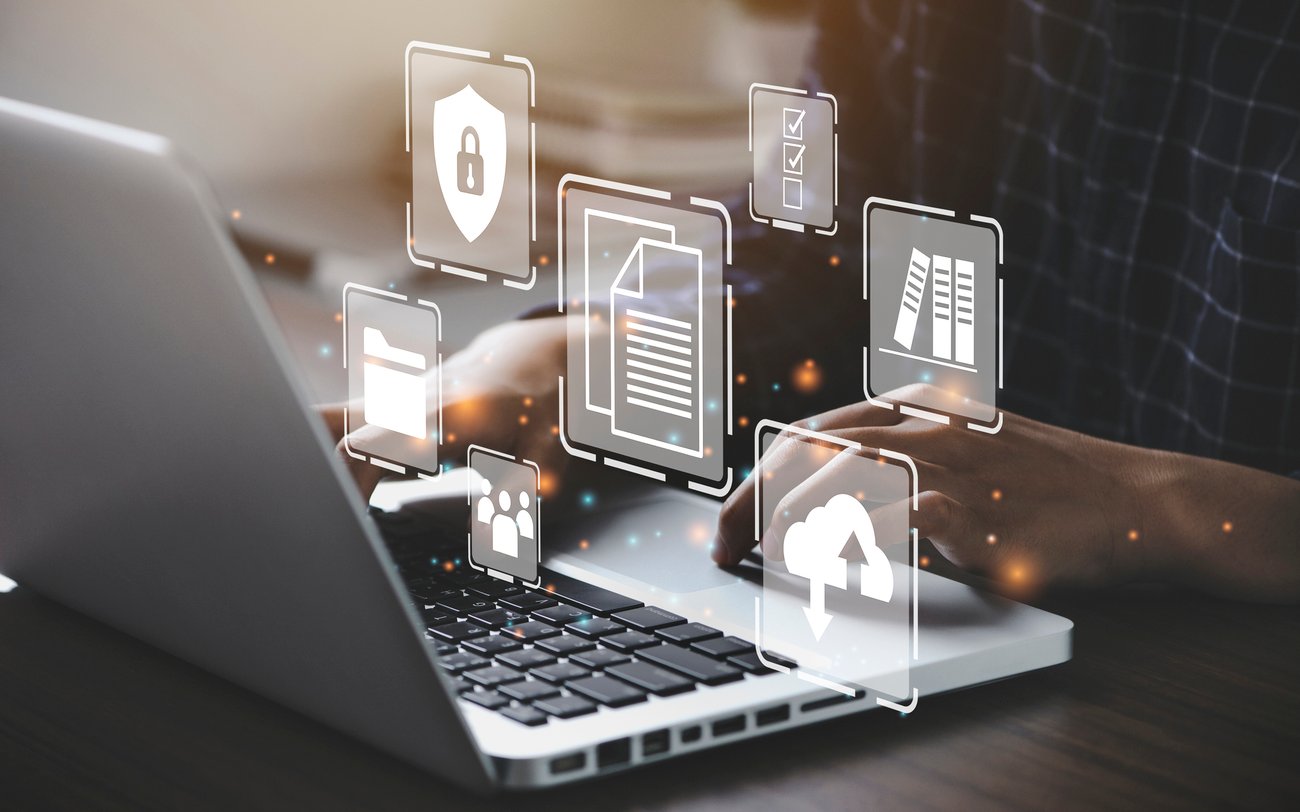 Man typing on laptop. There are various computer icons overlayed on the image. Icons include document, book, Cloud,
and security symbols.
