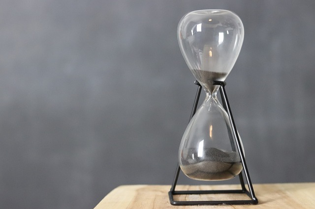 An hourglass timer filled with dark gray sand sitting on a tabletop.