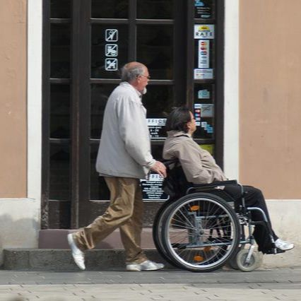 Man pushing a woman in a wheelchair down the street.