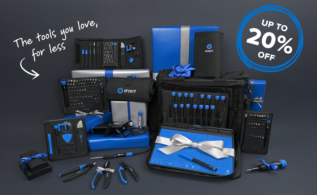 A large assortment of iFixit tools and kits arranged on a dark gray background, including the Pro Tech Toolkit, Manta Driver Kit, FixMat, Mandible pliers, FixHub Portable Soldering Station, and additional precision toolsets. Blue and silver wrapped gift boxes frame the display, with handwritten text reading “The tools you love, for less” and a blue circled badge showing “Up to 20% off,” creating a festive promotional scene.