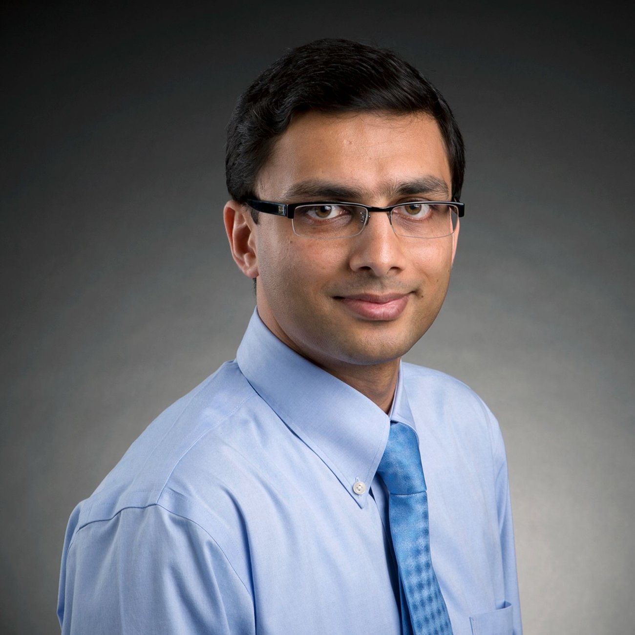 Photo of a man with glasses in a blue shirt with a blue tie