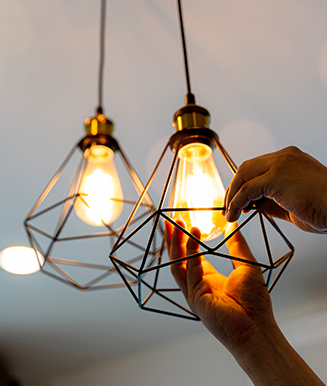 Photo of two light fixtures with the light bulbs on and hands screwing in one of the bulbs.