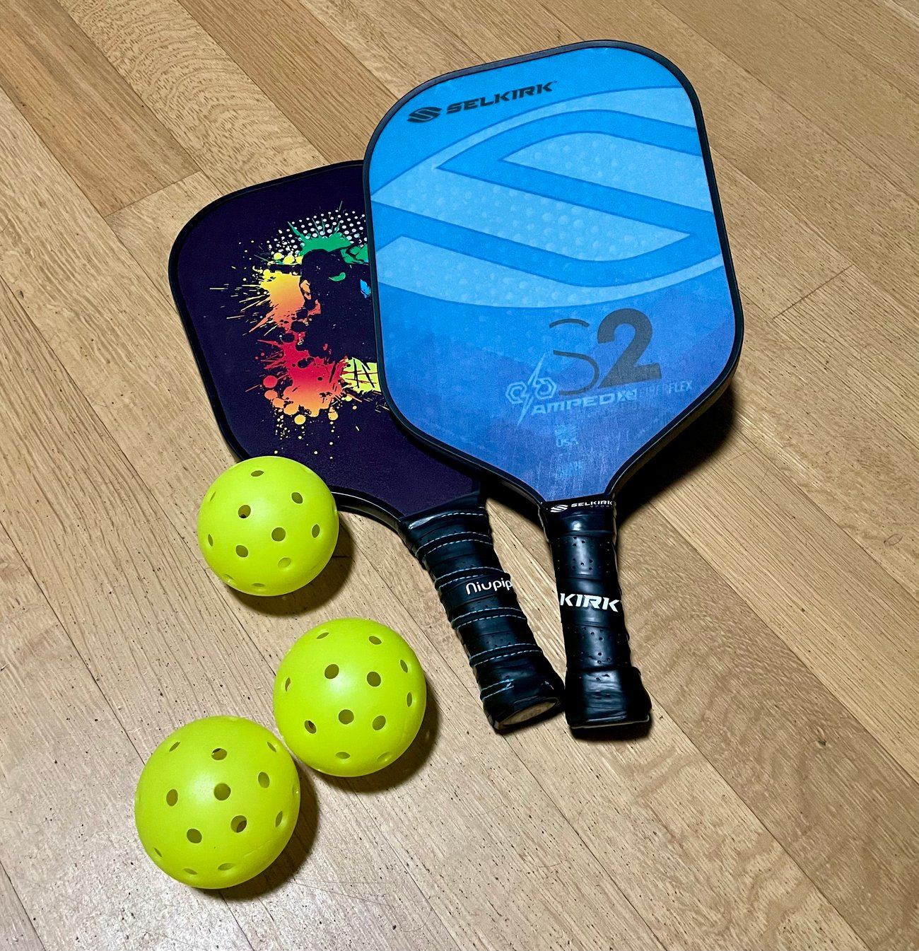 Photo of pickleball paddles and balls (via Wikimedia by E is for Ian) Photo of pickleball paddles and balls (via Wikimedia by E is for Ian)