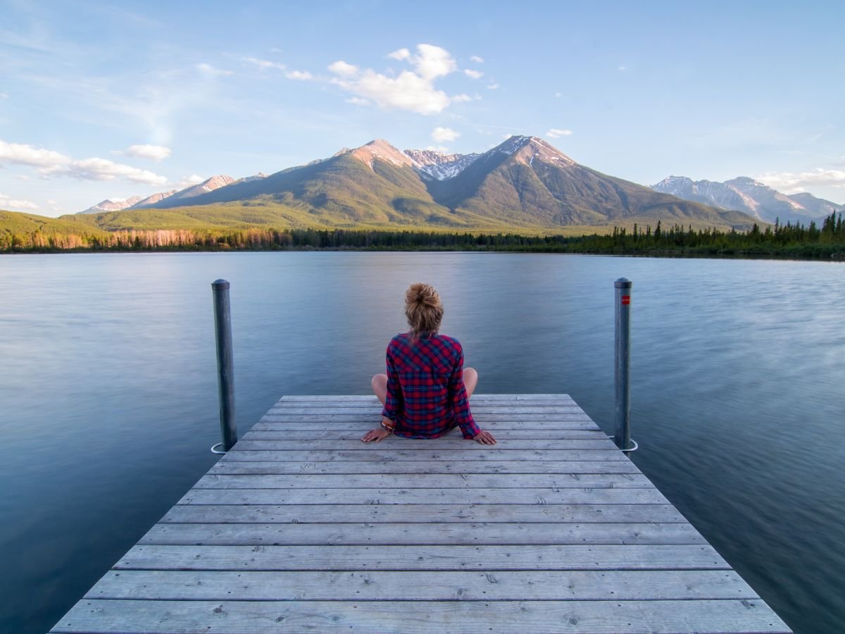 Person sat on a jetty overlooking water admiring view of mountains