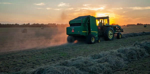 a farm tractor mowing in the sunset. Photo by Jed Owen on Unsplash