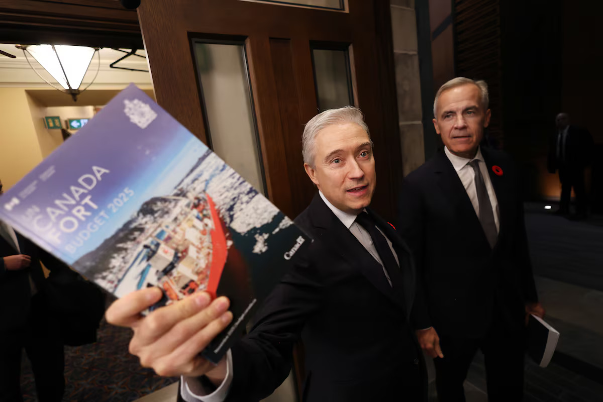 Finance minister François-Philippe Champagne holds a printed copy of the 2025 federal budget, standing beside Prime Minister Mark Carney