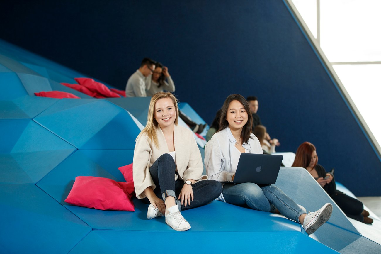 Two students sitting on blue stairs with laptops.
