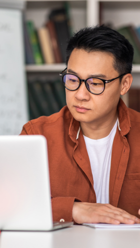 A person looks at a laptop while writing in a library.