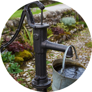An old-fashioned hand-powered well pump with a bucket full of water hanging
on it.