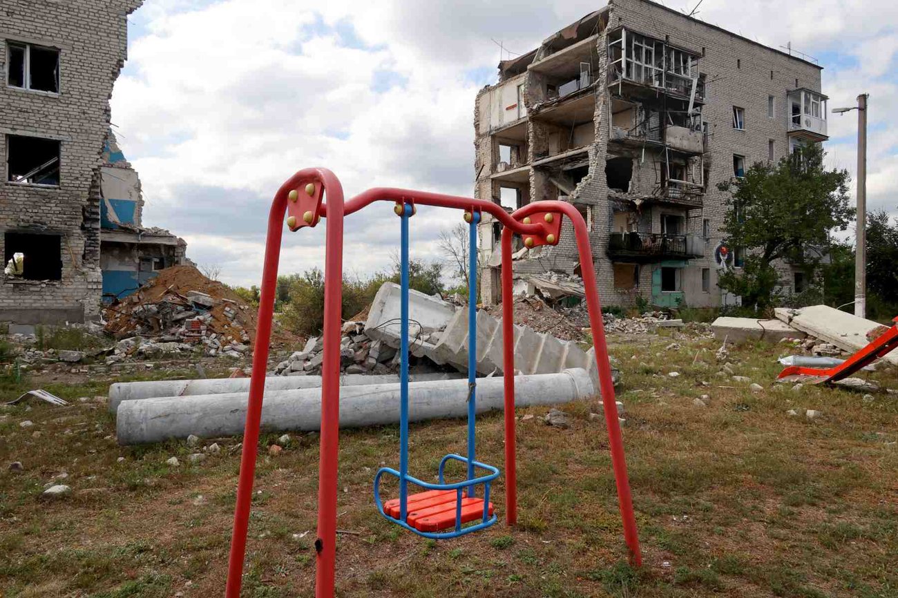 A red swing set is seen in front of two bombed out buildings.