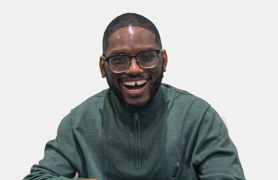 Image of a man withblack hair and a beard with glasses. He is wearing a pullover and smiling at the camera.