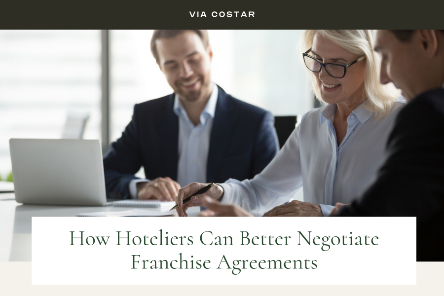 Via CoStar image: Smiling middle aged businesswoman signing paper contract at group meeting TEXT: "How Hoteliers Can Better Negotiate Franchise Agreements"