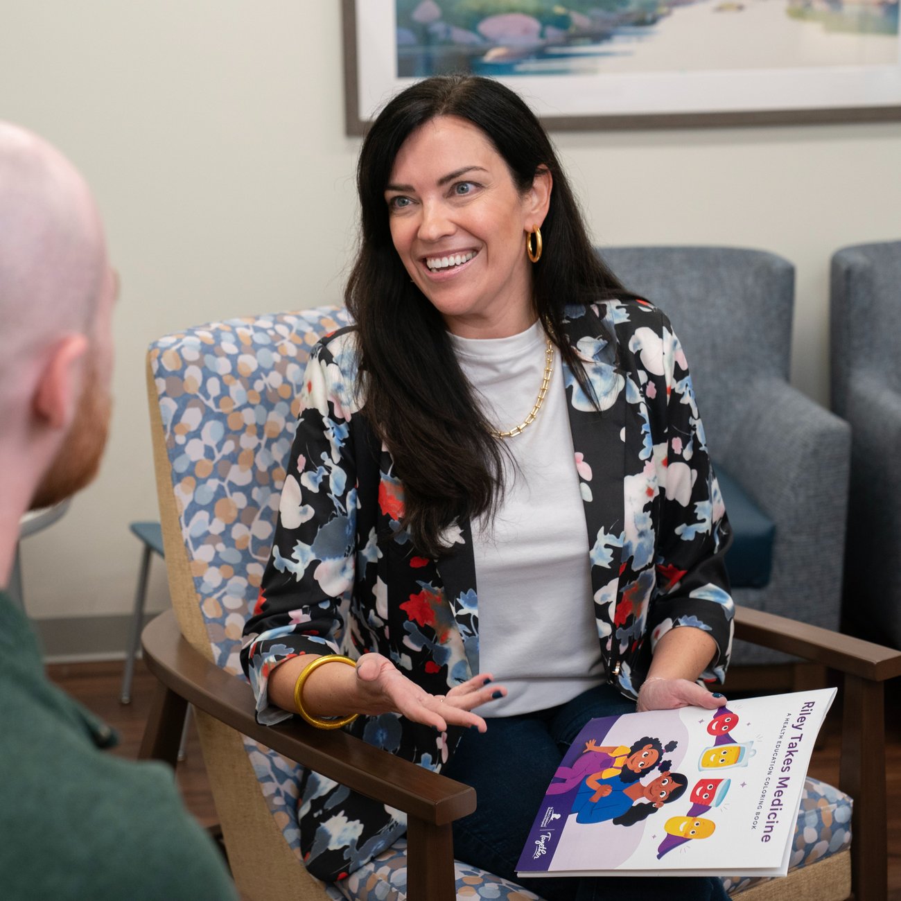 image of a women smiling in a floral cardigan holding a coloring book