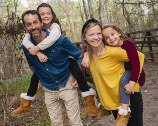 Image of a dad, mom, and two daughters with trees in the background