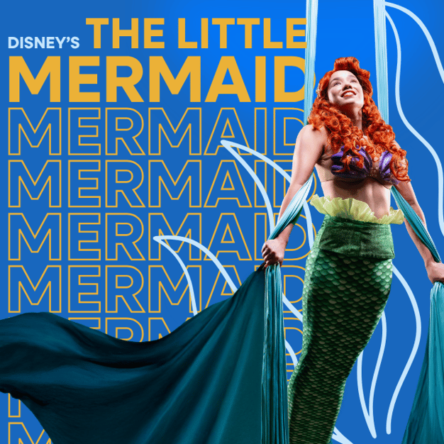 A smiling mermaid with flowing red hair and a green tail depicting swimming underwater by hanging on aerial silks