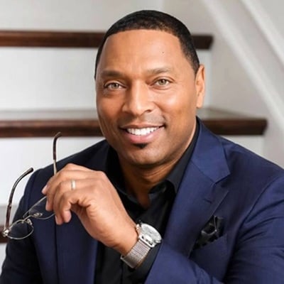 Smiling man in a navy suit holding eyeglasses