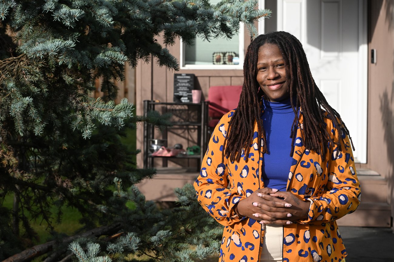 Smiling woman standing beside an evergreen tree outside a house