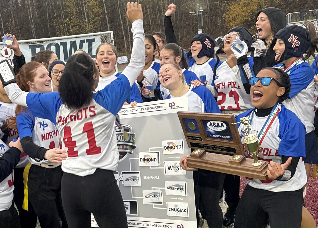 A jubilant girls' sports team celebrates with a championship trophy and bracket board