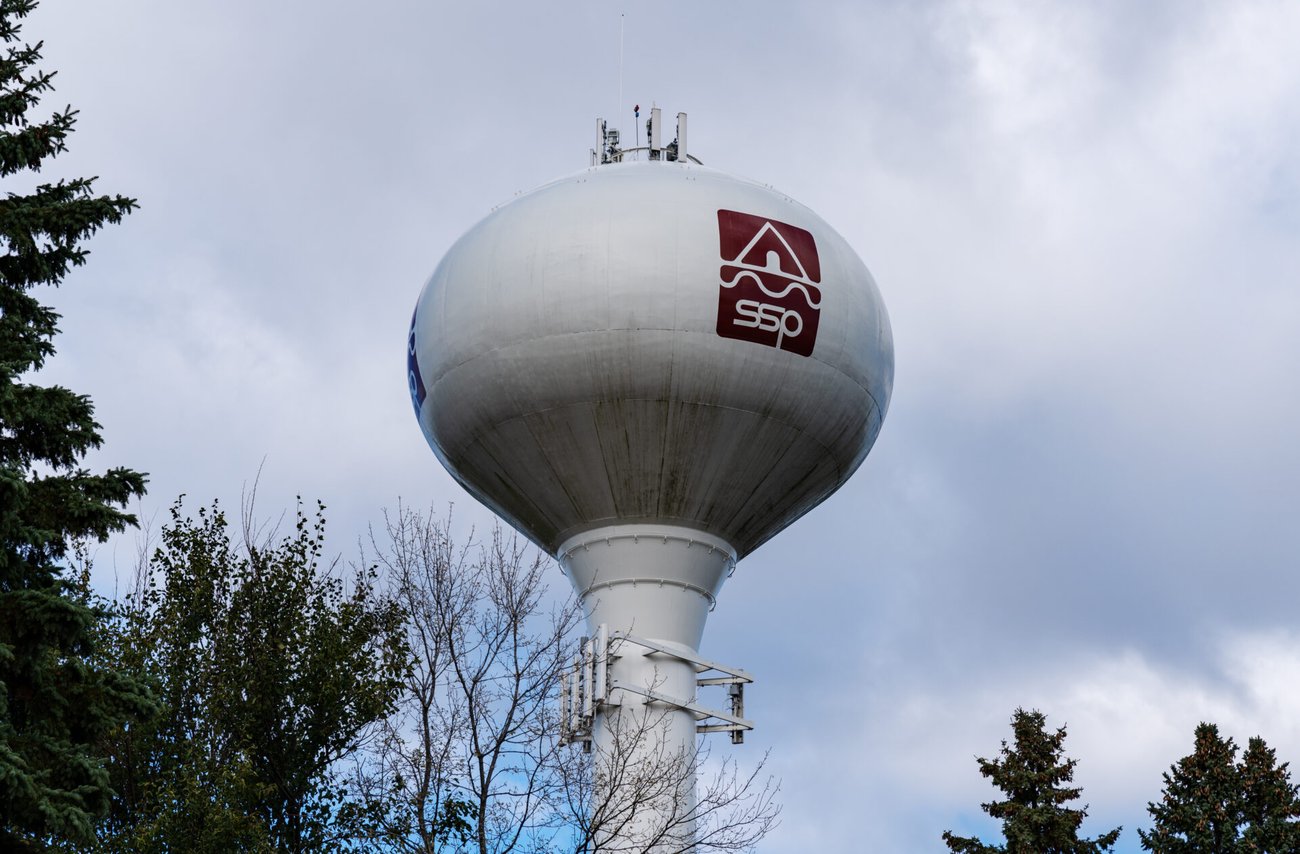 A large white water tower rising high above nearby trees