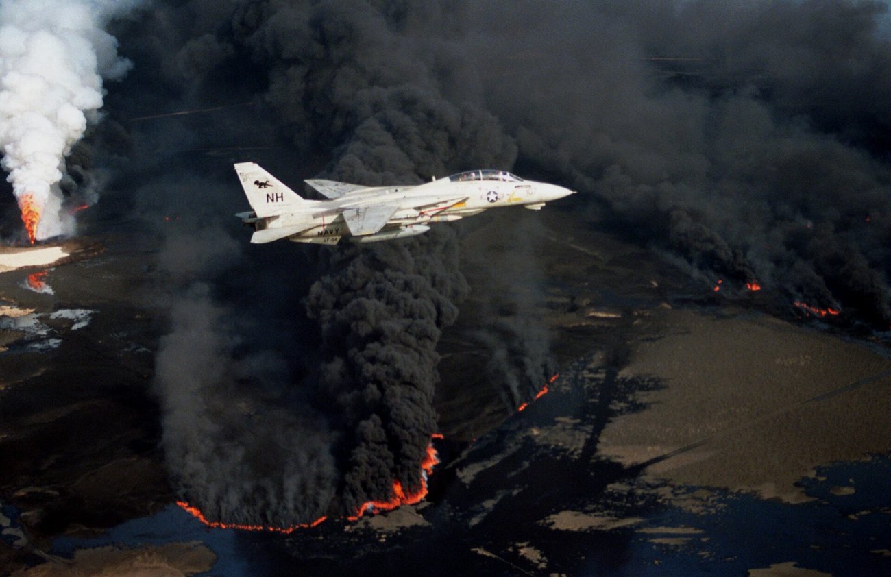 Fighter jet flies over a fire with billowing black smoke
