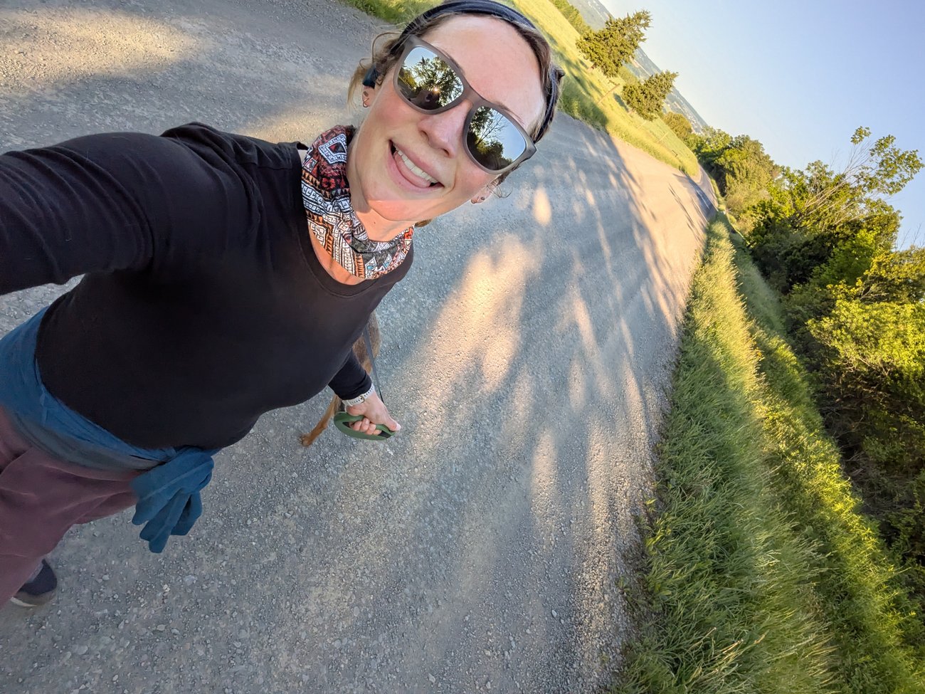 Abby walking along a dirt road wearing sunglasses and a neck gaiter.
